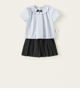 Détail de chemise bleue à col Claudine pour fille avec nœud et jupe plissée noire