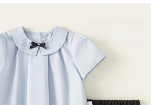 Détail d'une chemise fille bleu clair en coton avec col Claudine et petit nœud papillon noir