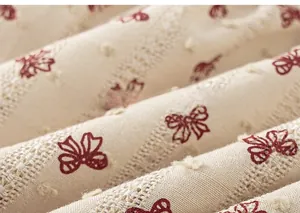 Close-up of beige cotton fabric with red bow prints and delicate embroidery textures