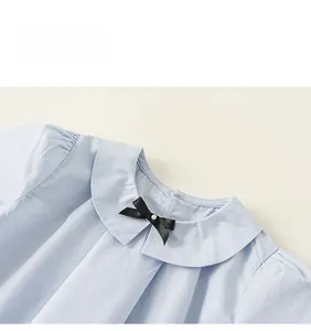 Détail du col Peter Pan sur chemise bleue pour fille avec nœud noir et perle
