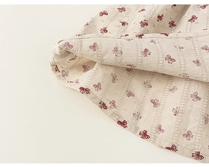 Detailed view of white fabric with red bow print and delicate swiss dot embroidery texture