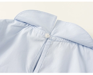 Détail de la chemise bleu clair montrant le bouton au col arrière et la texture du tissu