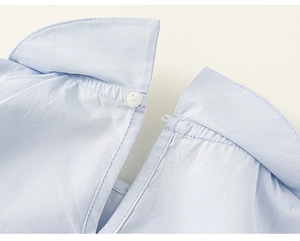 Détail de l'encolure d'une chemise fille bleu clair avec bouton blanc et fente en goutte
