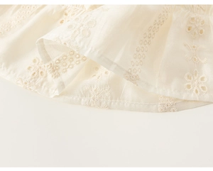 Detail eines cremefarbenen Kleides mit floraler Lochstickerei und Rüschensaum