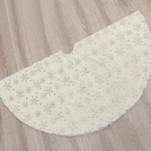 White plush Christmas tree skirt with gold sequined snowflake patterns on wood floor