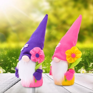 Pair of plush garden gnomes with flower hats on a white wooden deck in a sunny garden