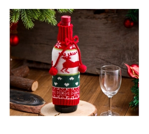 Close-up of knitted wine bottle cover with red reindeer, snowflakes and fluffy pom-poms