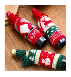 Macro detail of knitted Christmas wine bottle covers with pom-pom ties on a wooden surface