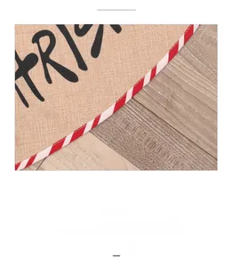 Close-up of burlap Christmas tree skirt with red striped piping and holiday typography
