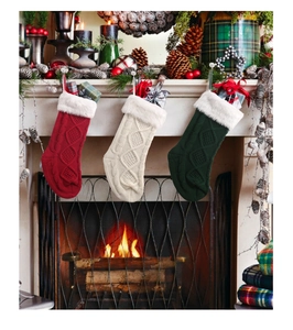 Drei gestrickte Weihnachtsstrümpfe mit weißem Kunstfellbesatz an einem Kamin im Detail