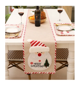 Close-up of burlap Christmas table runner with Santa Claus embroidery and pom-poms