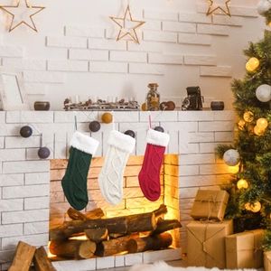 Drei plüschige Strick-Weihnachtssocken in Rot, Grün und Weiß hängen an einem Kamin
