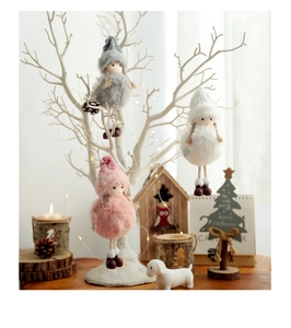 Close-up of three plush Christmas angel dolls with knit hats hanging on a festive tree