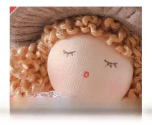 Close-up of handmade Christmas angel doll face with embroidered eyes and grey knit hat