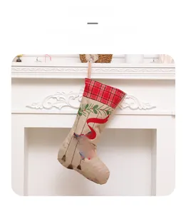 Detail of burlap Christmas stocking with red plaid cuff and Welcome embroidery hanging on fireplace