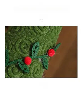 Close-up of green knitted gnome hat with spiral texture, felt leaves and red pom poms
