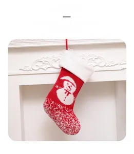 Detail of red knitted Christmas stocking with white snowman pattern on fireplace