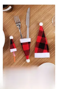 Close-up of red and black buffalo plaid mini Christmas hats on wooden table for cutlery