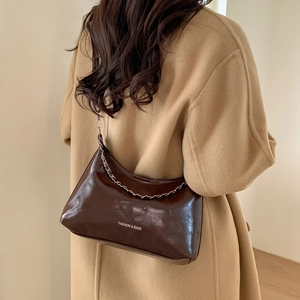 Chic sac hobo en cuir verni marron foncé avec chaîne argentée porté par une femme