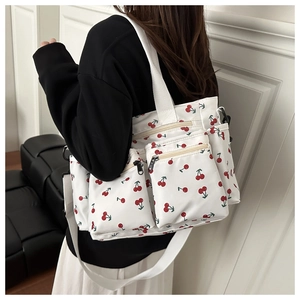 Model wearing a white handbag with red cherry print featuring three front zipper pockets