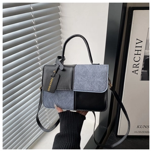Detail of color-block square bag showing blue denim texture and black leather tag