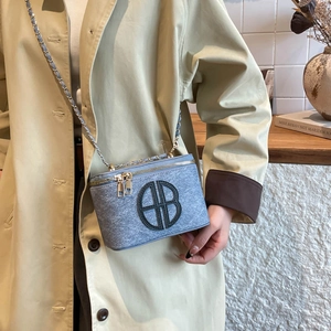 Blue-grey tweed cylindrical chain bag with circular BB logo shown on a beige trench coat