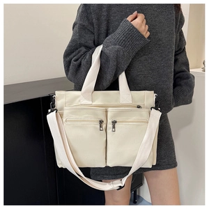 Detail view of cream canvas tote bag with functional zippers and adjustable shoulder strap