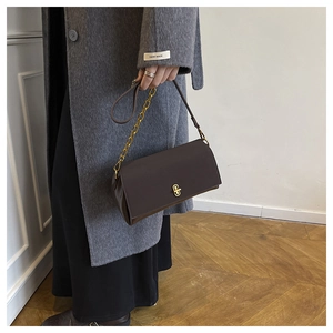 Detail of dark brown saddle bag featuring gold oval twist lock and metal chain handle