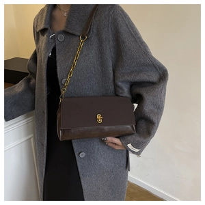 Detail of a dark brown saddle bag with golden twist lock and chain leather strap