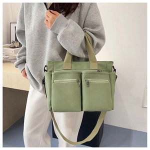 Detail of avocado green canvas tote bag featuring multiple front zip pockets and shoulder strap