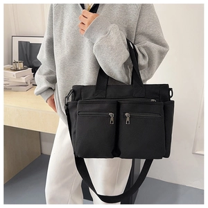 Detail of black canvas tote bag with front zipper pockets and adjustable shoulder strap