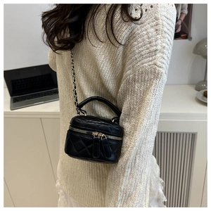 Model wearing a black quilted mini chain bag with gold hardware in a modern home setting