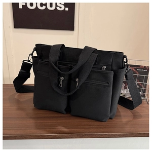 Detail of black canvas tote bag showing dual front zip pockets and wide woven shoulder strap