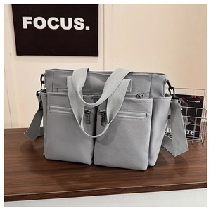Detailed view of light gray multi-pocket canvas tote with dual zipper pockets on a table