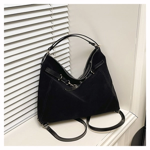 Détail d'un sac hobo en daim noir avec œillets argentés et bandoulière en cuir sur un rebord