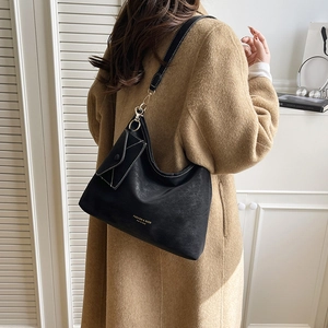 Classic black suede tote bag with gold lettering shown on a model in wool coat