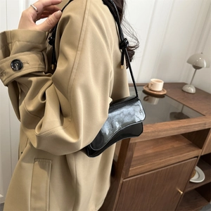 Minimalist black glossy shoulder bag with wavy bottom and knot detail on shoulder strap
