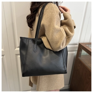 Side view of a large black matte leather tote bag worn by a model in a minimalist interior