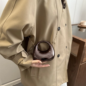 Mini sac de soirée métallisé demi-lune avec chaîne dorée porté sur un trench-coat
