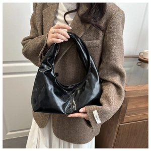 Detail of glossy black vintage shoulder bag held by model wearing a brown tweed blazer