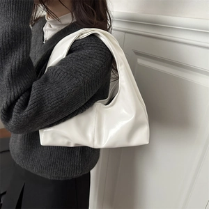 Minimalist white patent leather hobo bag with wide shoulder strap worn by a model