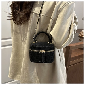 Detail shot of a black leopard print crossbody bag with gold chain strap on cream coat