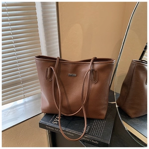 Detailed close-up of brown litchi grain leather tote bag with elegant metal logo plaque