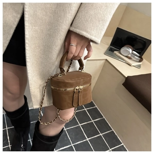 Detail of suede crossbody bag featuring a boxy structure, round top handle, and chain strap