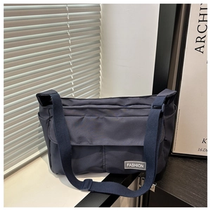 Detail of navy messenger bag with adjustable strap and fashion label on front