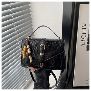 Detail view of black crocodile pattern faux leather handbag with retro bead charm