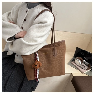 Detailed close-up of brown leopard print tote bag with plush puppy charm on leather handle
