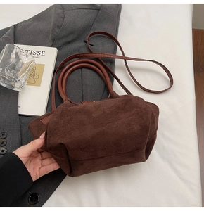 Detail of dark brown suede handbag with leather handle placed on grey blazer