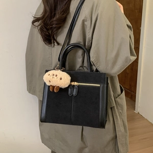 Black textured suede tote bag with plush biscuit charm and crossbody strap