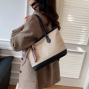 Large beige canvas tote bag with black leather trim and decorative silk scarf detail